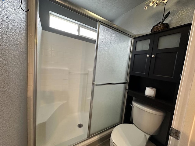 bathroom with toilet, a textured ceiling, and a shower with shower door