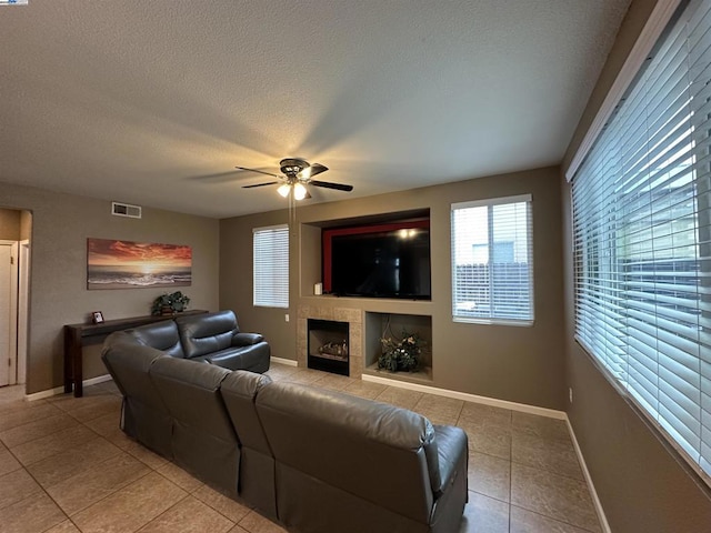 living room with a tiled fireplace, light tile patterned floors, a textured ceiling, and ceiling fan