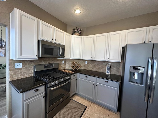 kitchen featuring light tile patterned floors, appliances with stainless steel finishes, dark stone countertops, tasteful backsplash, and white cabinets