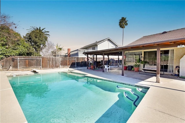 pool at dusk featuring a diving board and a patio area