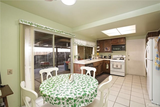 kitchen featuring light tile patterned flooring, a skylight, sink, kitchen peninsula, and white appliances