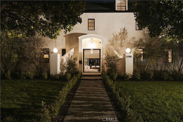 exterior entry at night featuring a lawn