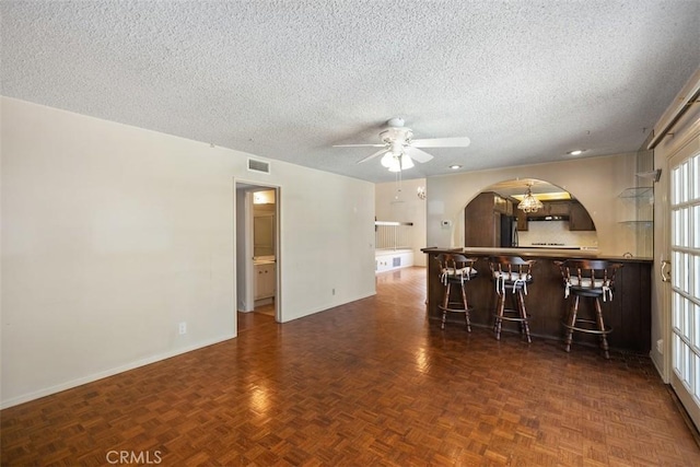 kitchen with ceiling fan, a textured ceiling, dark parquet flooring, and a breakfast bar area