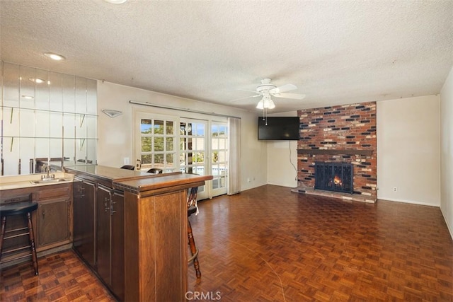 kitchen with a fireplace, kitchen peninsula, dark parquet floors, ceiling fan, and a textured ceiling