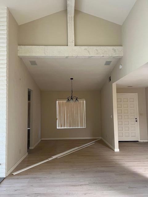 unfurnished dining area with an inviting chandelier, hardwood / wood-style flooring, and high vaulted ceiling