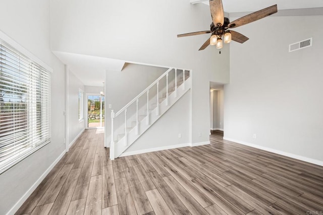 unfurnished living room featuring ceiling fan with notable chandelier, a towering ceiling, and hardwood / wood-style floors