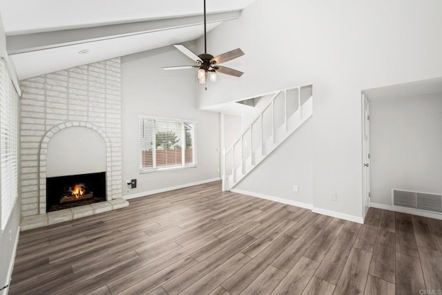 unfurnished living room featuring high vaulted ceiling, beamed ceiling, ceiling fan, a fireplace, and hardwood / wood-style floors