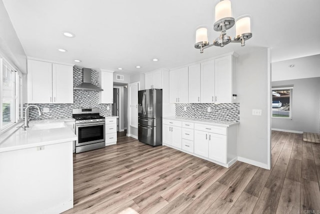 kitchen with wall chimney exhaust hood, sink, white cabinetry, appliances with stainless steel finishes, and hardwood / wood-style flooring