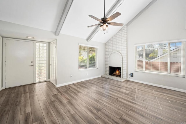 unfurnished living room featuring high vaulted ceiling, a brick fireplace, light hardwood / wood-style flooring, ceiling fan, and beam ceiling