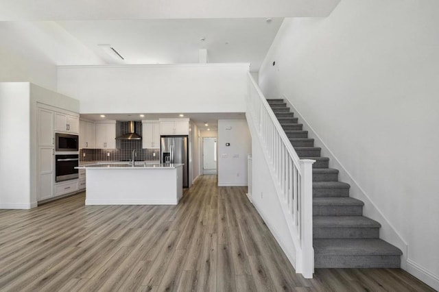 kitchen with appliances with stainless steel finishes, sink, white cabinets, a kitchen island with sink, and wall chimney range hood