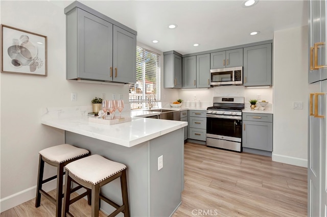 kitchen featuring appliances with stainless steel finishes, gray cabinetry, light hardwood / wood-style floors, a kitchen bar, and kitchen peninsula