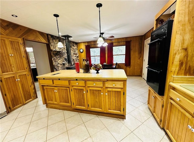 kitchen with double oven, hanging light fixtures, wooden walls, a center island, and a wood stove