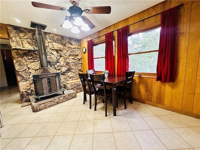 dining room featuring ceiling fan, wood walls, light tile patterned floors, and a wood stove