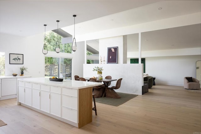 kitchen featuring hanging light fixtures, a kitchen island, light hardwood / wood-style floors, white cabinets, and a kitchen bar