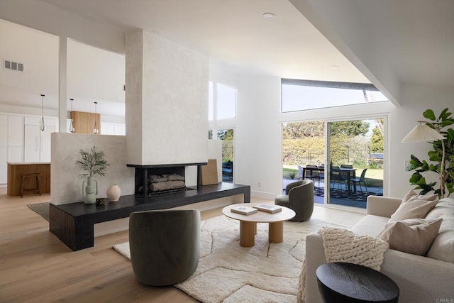 living room featuring a large fireplace, a towering ceiling, and light wood-type flooring