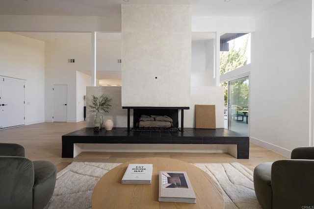 living room featuring a tiled fireplace, a towering ceiling, and hardwood / wood-style floors