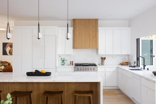 kitchen featuring decorative light fixtures, white cabinetry, sink, a breakfast bar area, and stove