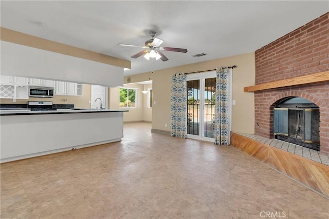 kitchen with sink, ceiling fan, stainless steel appliances, a fireplace, and white cabinets