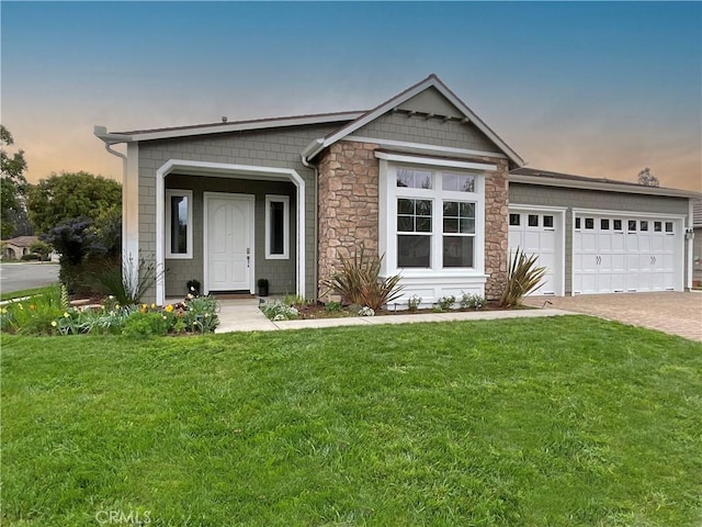 view of front facade with stone siding, an attached garage, decorative driveway, and a yard