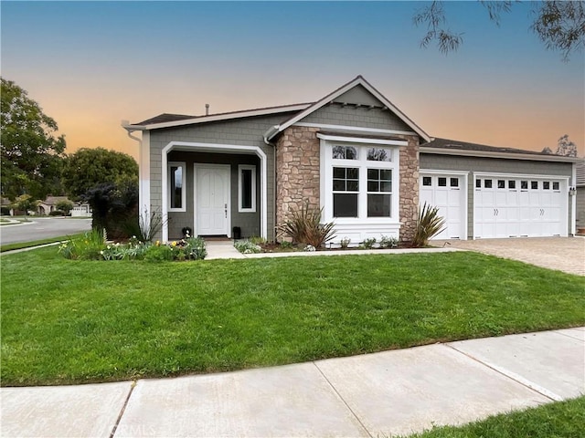 view of front facade featuring stone siding, a yard, decorative driveway, and an attached garage