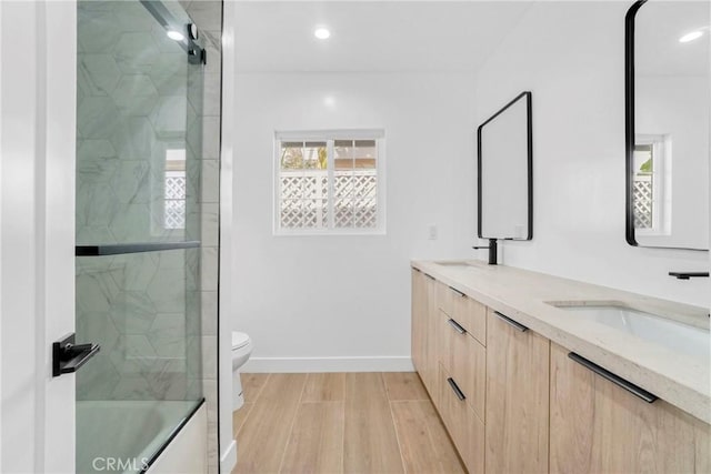 bathroom with toilet, wood finished floors, a sink, baseboards, and double vanity