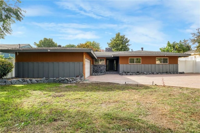 view of front of property with a garage, stone siding, a front lawn, and fence