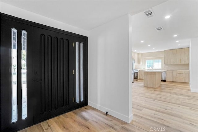 foyer entrance with visible vents, light wood-style flooring, and baseboards