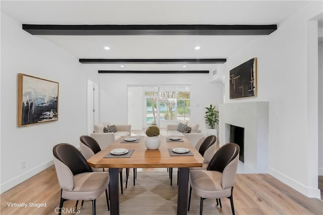 dining space featuring beam ceiling, a fireplace, light wood-style flooring, and baseboards