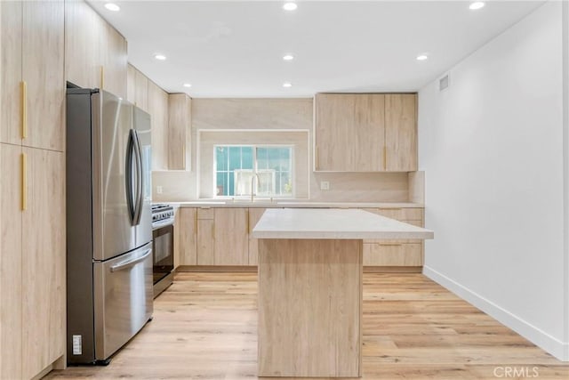 kitchen featuring light brown cabinets, stainless steel appliances, light wood-style floors, light countertops, and a center island