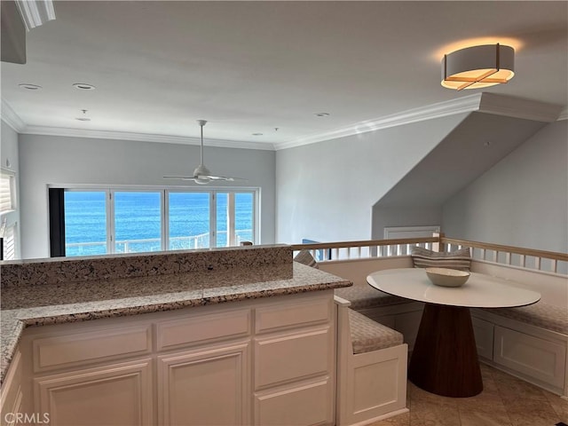 kitchen with a water view, white cabinetry, hanging light fixtures, ornamental molding, and light stone countertops