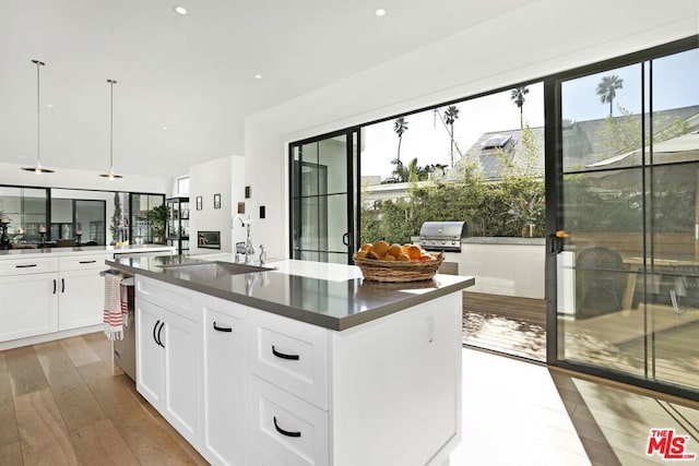 kitchen featuring pendant lighting, white cabinets, a kitchen island with sink, plenty of natural light, and light hardwood / wood-style flooring