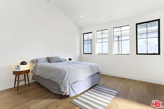 bedroom featuring lofted ceiling, hardwood / wood-style floors, and multiple windows