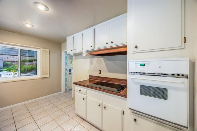 kitchen with under cabinet range hood, light tile patterned floors, white oven, white cabinets, and black electric cooktop