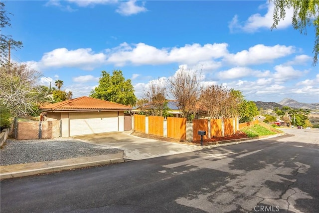 view of front of property featuring a detached garage, a fenced front yard, a tile roof, stucco siding, and a mountain view