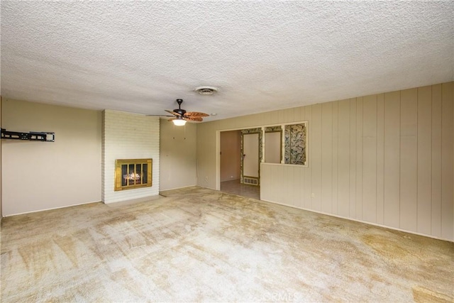 unfurnished living room featuring visible vents, a ceiling fan, a textured ceiling, carpet flooring, and a brick fireplace