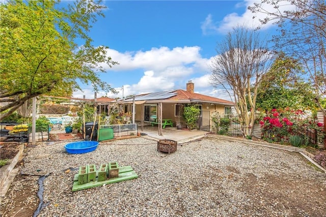 back of house with fence, a chimney, a fire pit, a patio area, and roof mounted solar panels