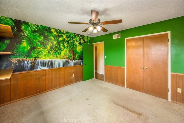 unfurnished bedroom with a wainscoted wall, visible vents, wood walls, and a textured ceiling