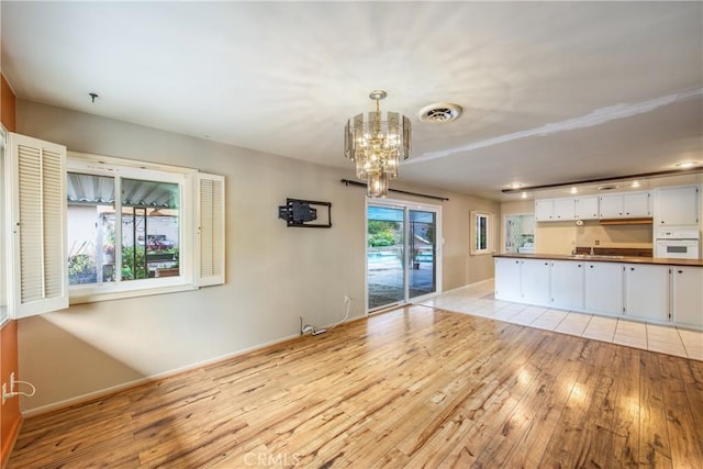 unfurnished living room featuring an inviting chandelier, light wood-style flooring, baseboards, and visible vents