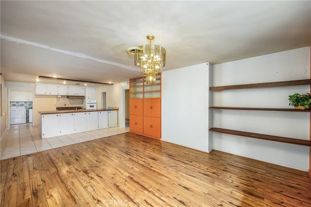 kitchen with washing machine and clothes dryer, dark countertops, oven, light wood-type flooring, and white cabinetry