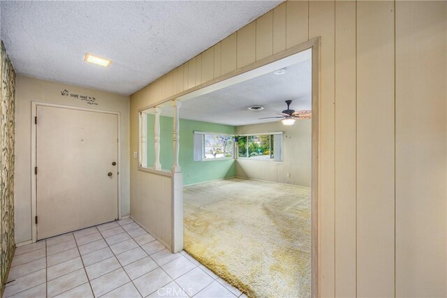 entryway featuring wooden walls, light tile patterned floors, a ceiling fan, a textured ceiling, and light colored carpet