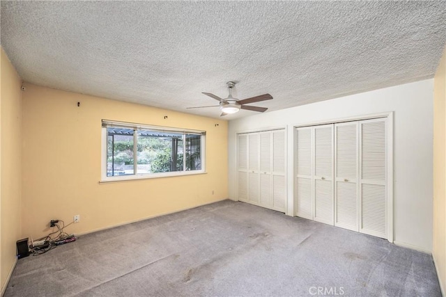 unfurnished bedroom featuring multiple closets, a textured ceiling, carpet floors, and ceiling fan