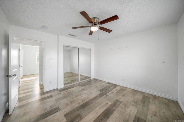 unfurnished bedroom featuring ceiling fan, light hardwood / wood-style flooring, a closet, and a textured ceiling