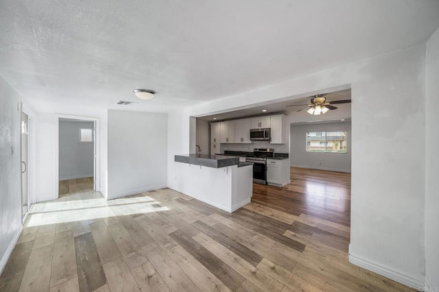 kitchen with a breakfast bar area, appliances with stainless steel finishes, white cabinetry, light hardwood / wood-style floors, and kitchen peninsula