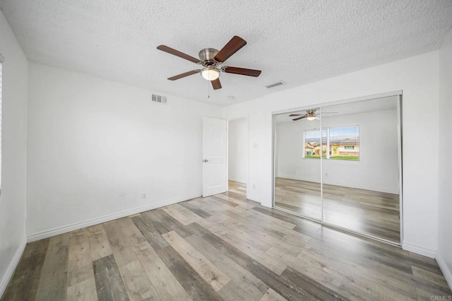 unfurnished bedroom featuring ceiling fan, a closet, a textured ceiling, and light wood-type flooring