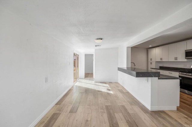 kitchen featuring appliances with stainless steel finishes, a breakfast bar area, white cabinets, light hardwood / wood-style floors, and kitchen peninsula