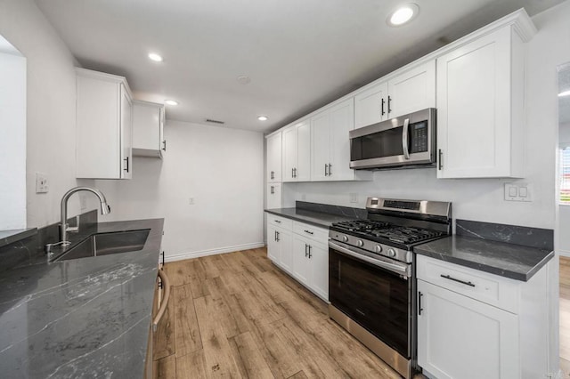 kitchen with sink, light hardwood / wood-style flooring, appliances with stainless steel finishes, white cabinetry, and dark stone countertops