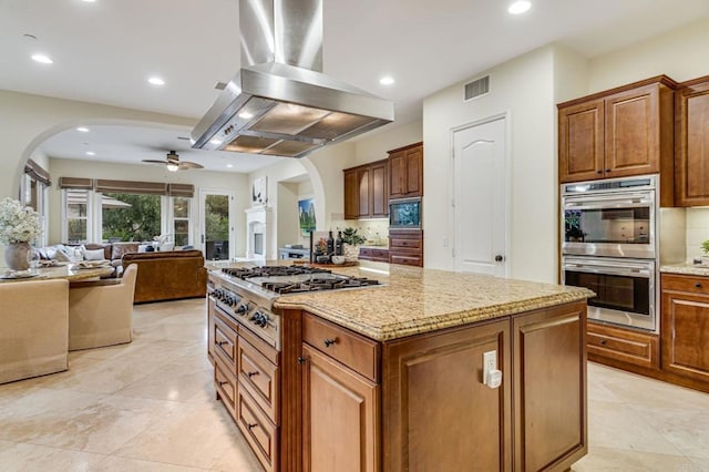 kitchen featuring appliances with stainless steel finishes, light stone countertops, island exhaust hood, decorative backsplash, and a kitchen island