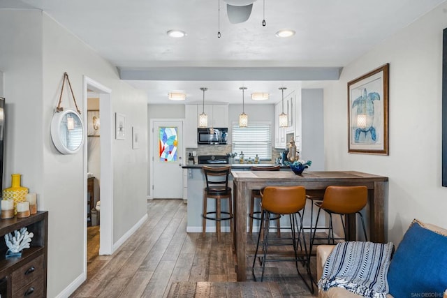 kitchen featuring hardwood / wood-style floors, decorative light fixtures, tasteful backsplash, white cabinetry, and a kitchen breakfast bar