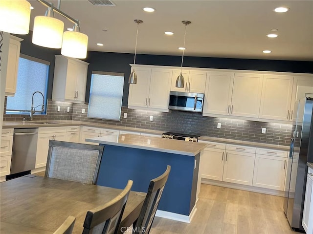 kitchen featuring stainless steel appliances, sink, white cabinets, and decorative light fixtures