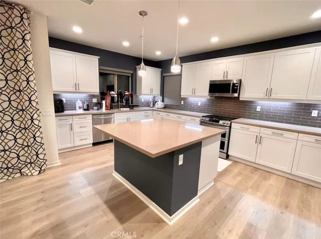 kitchen with a kitchen island, appliances with stainless steel finishes, pendant lighting, white cabinets, and light hardwood / wood-style floors